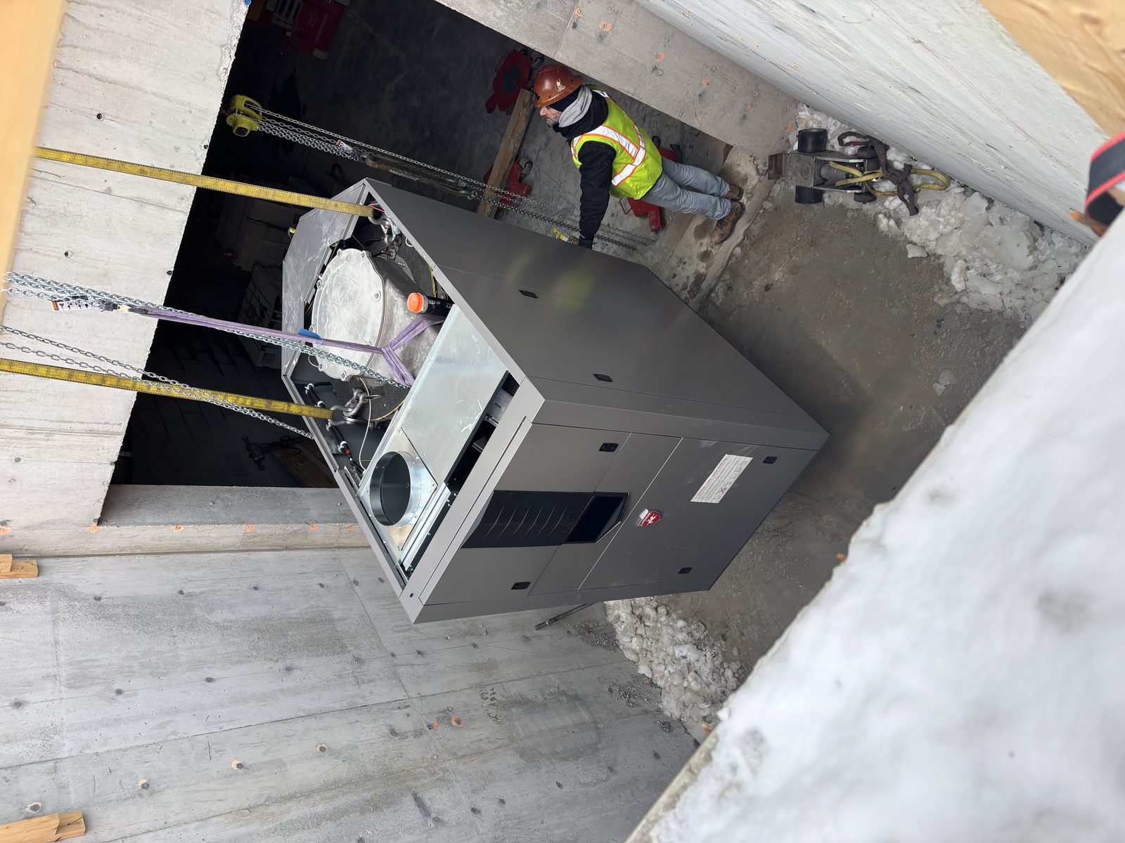 A crane lowering an HVAC unit through a rooftop opening on a Chicago jobsite