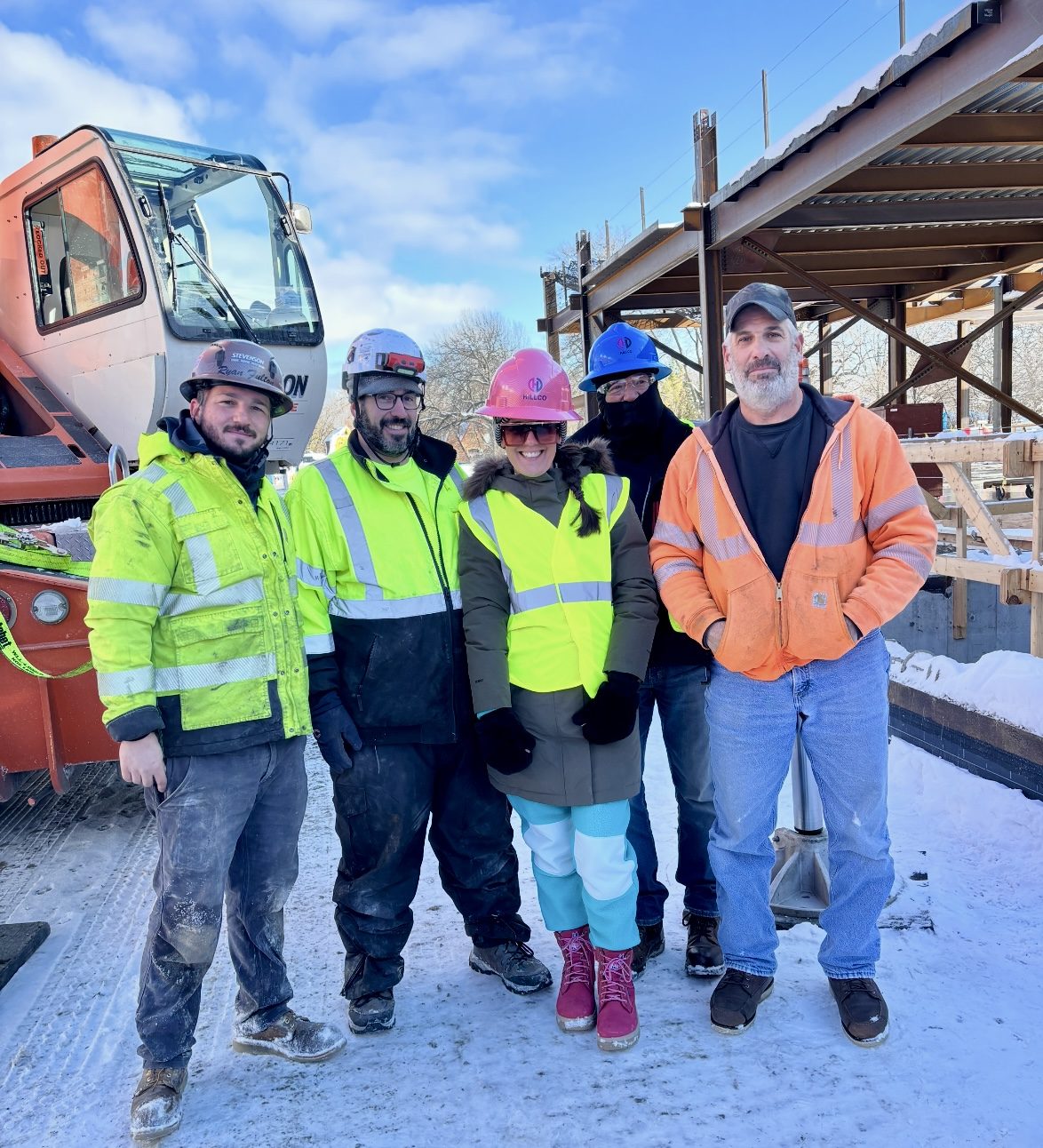 Nikki Liddy in a pink hard hat with a jobsite crew in high-visibility gear